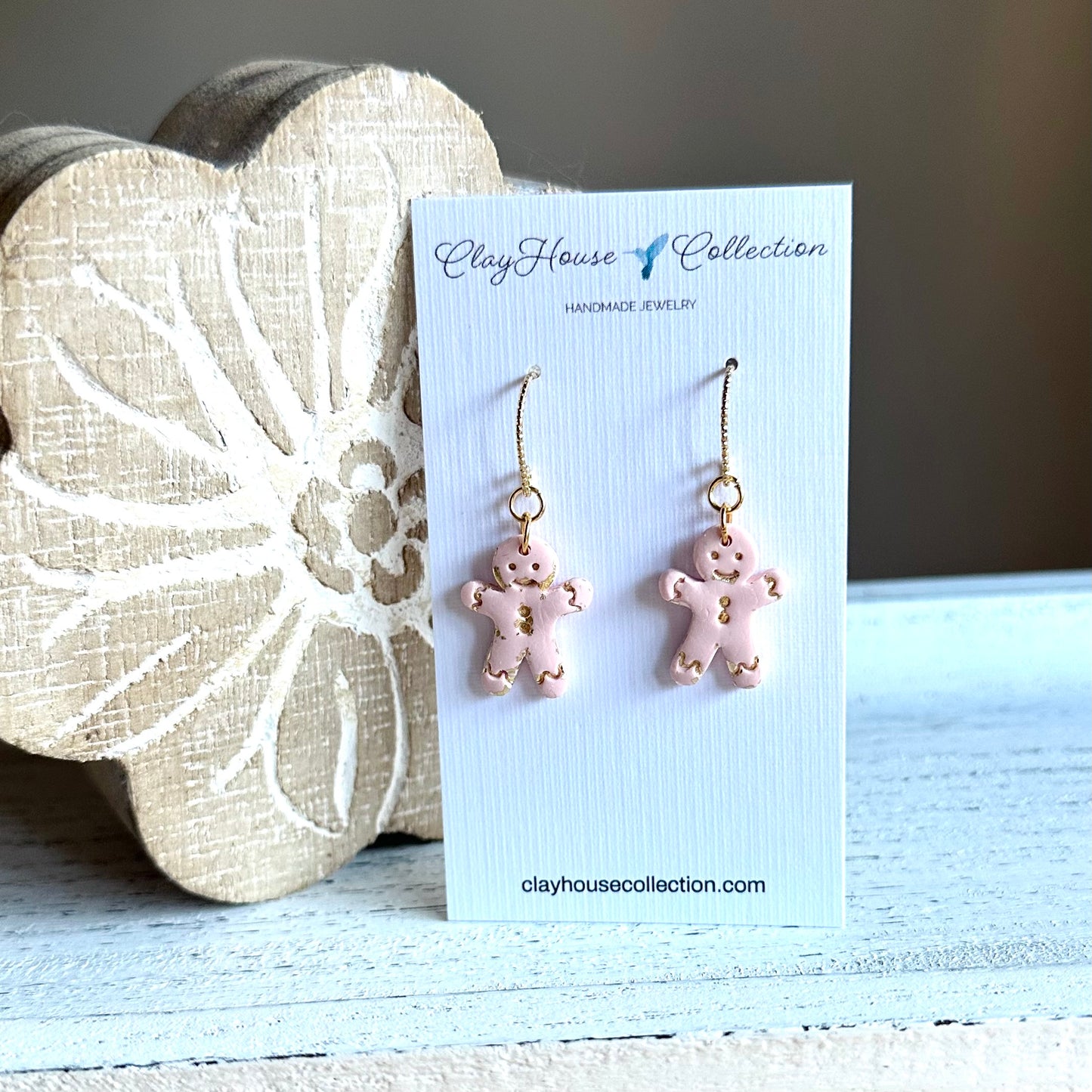 Pink gingerbread man earrings on a Clay House Collection card with a decorative stone background.