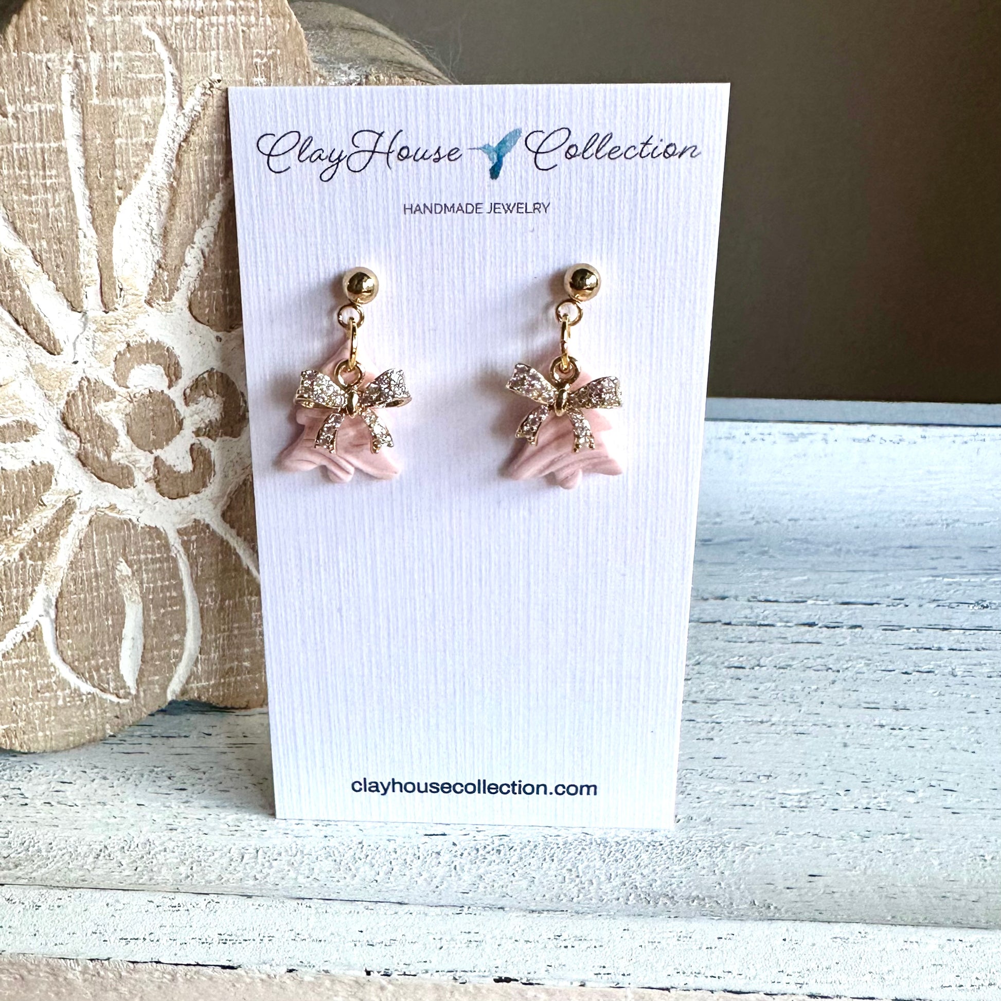 Pair of pink bow-shaped earrings on a ClayHouse Collection card.