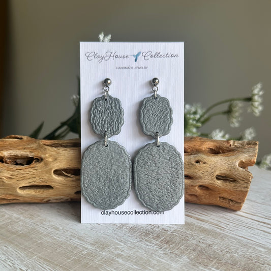 Gray earrings on a Clay House Collection card with driftwood and flowers in the background