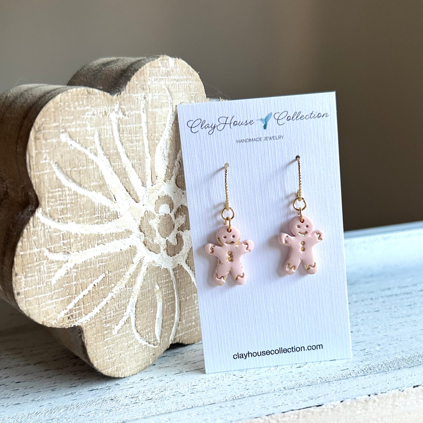 Pink gingerbread man earrings on a ClayHouse Collection card with a wooden block in the background.