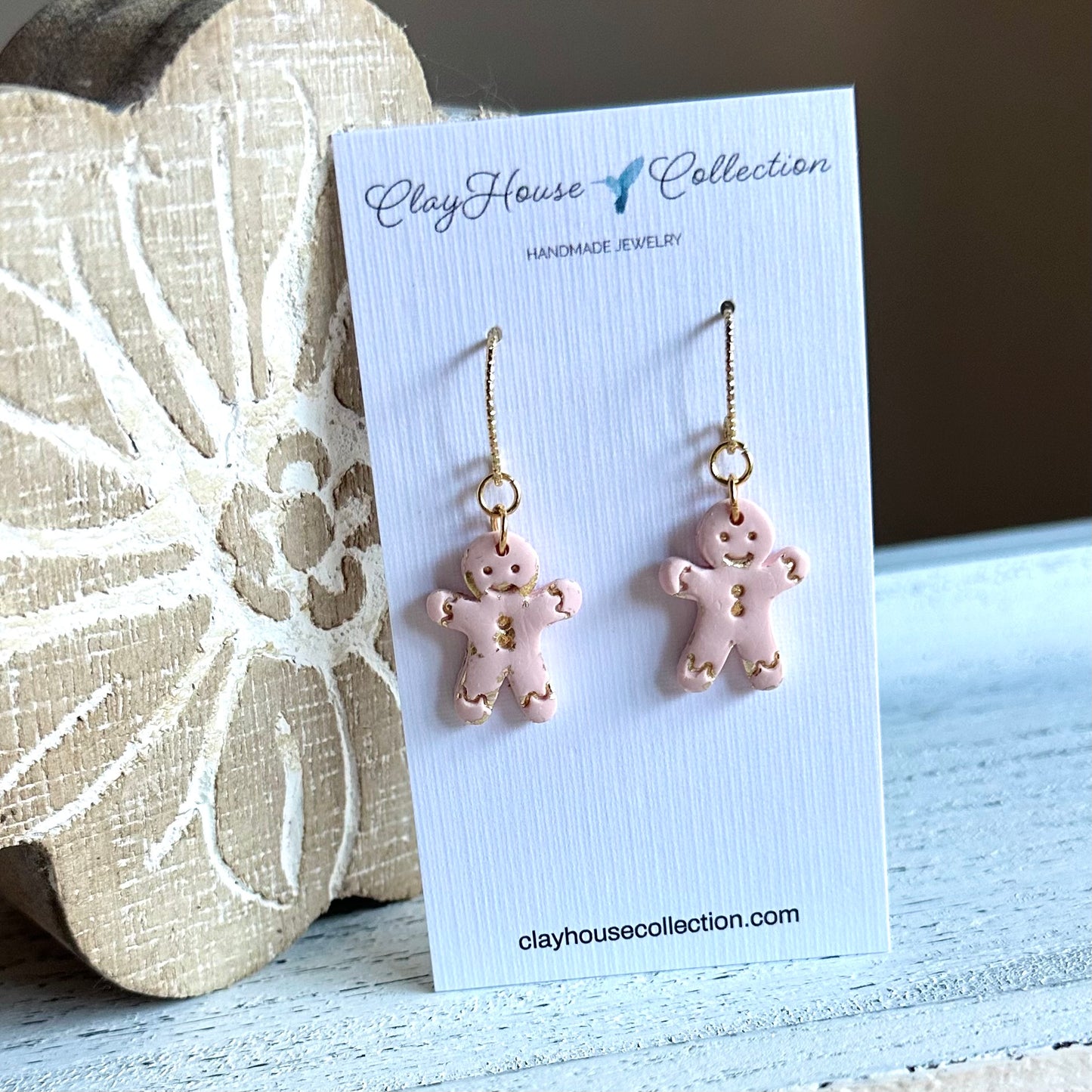 Pink gingerbread man earrings on a Clay House Collection card with decorative background