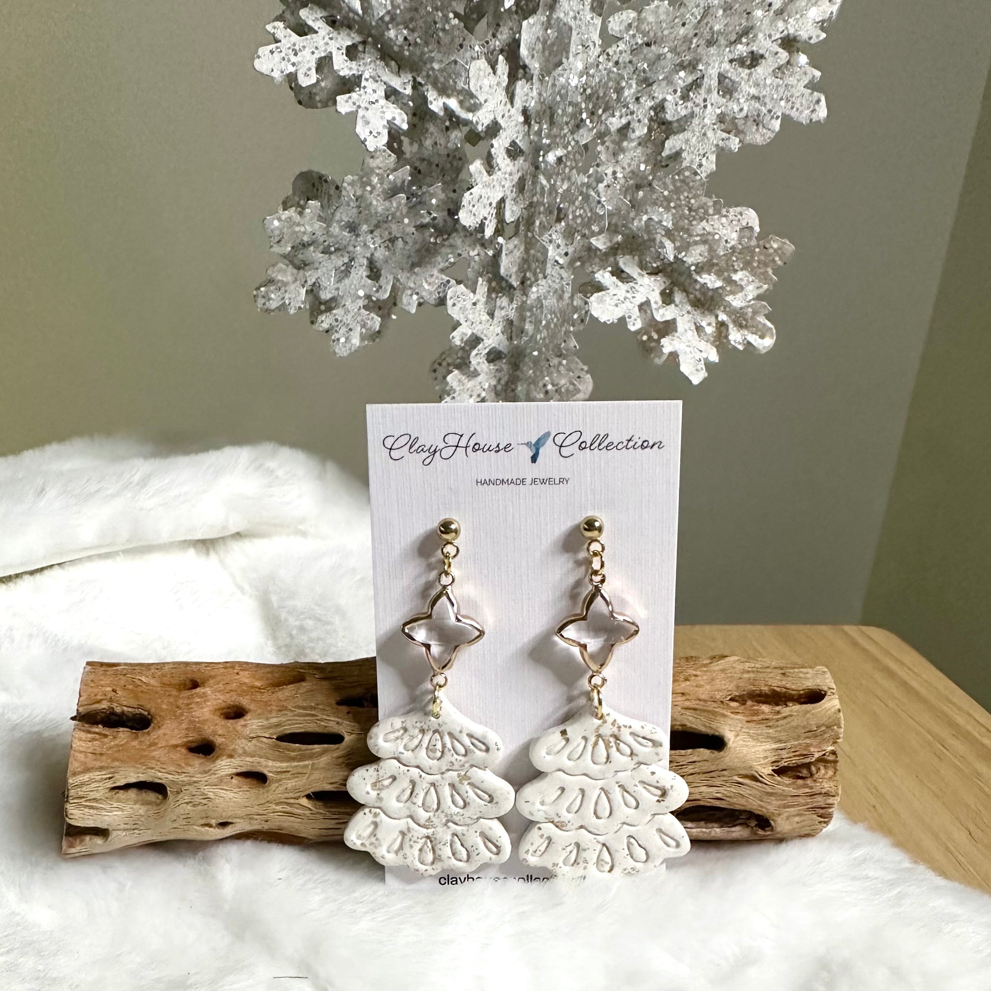 White lace-style earrings on a card with 'CleyHouse Collection' branding, displayed on a wooden block with a white fabric background.