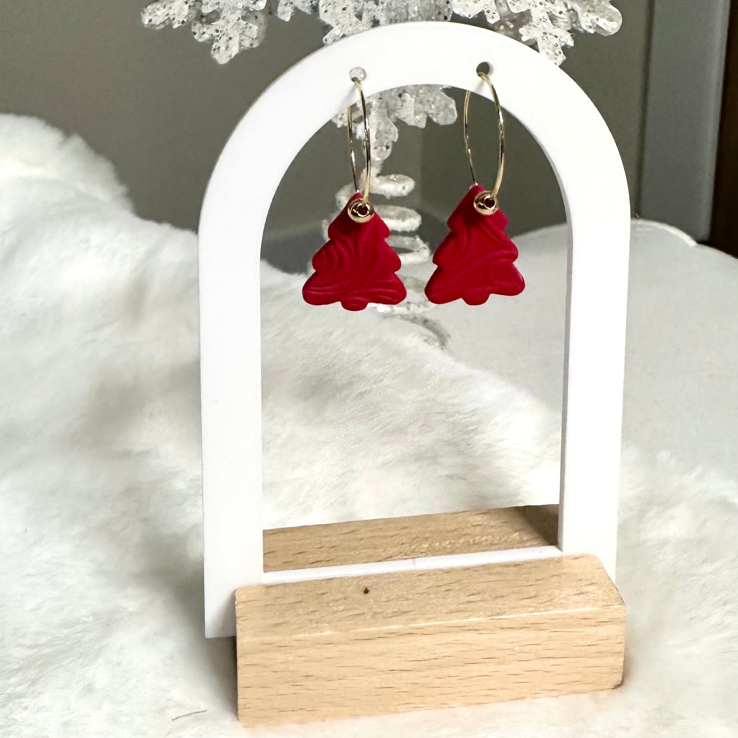 Red heart-shaped earrings on a white and wooden stand with a soft white background