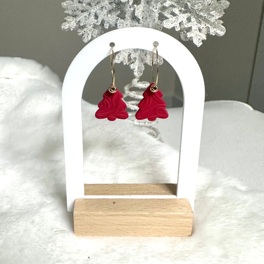 Red Christmas tree-shaped earrings on a white stand with a snowy background