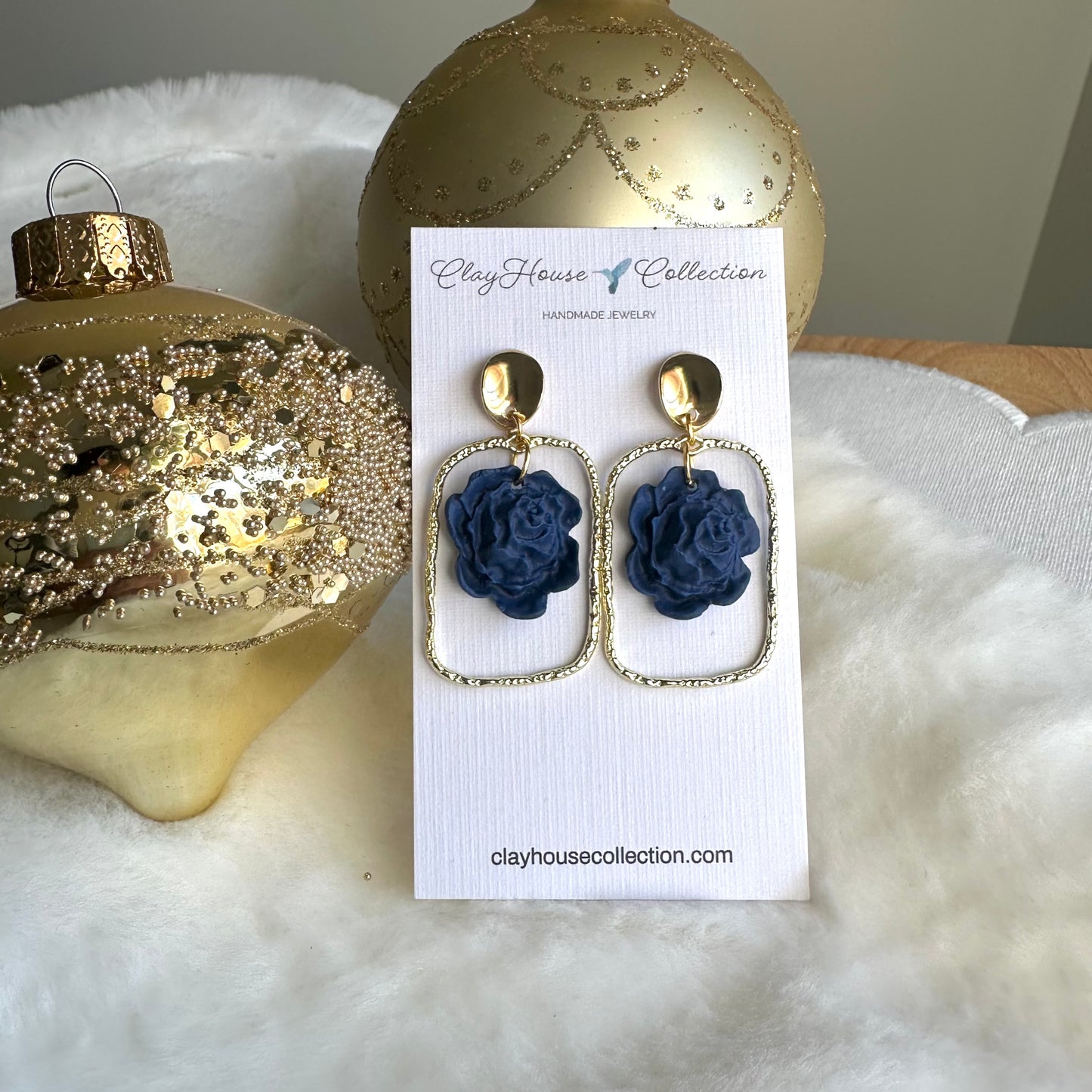 Navy blue flower earrings on a white card with gold ornaments in the background