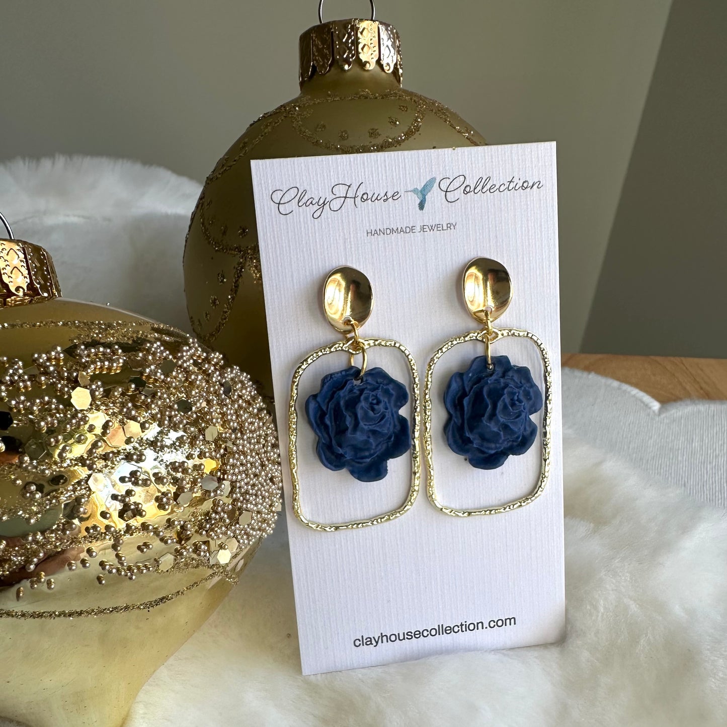 Navy blue flower earrings on a ClayHouse Collection card with gold accents, placed against a neutral background.