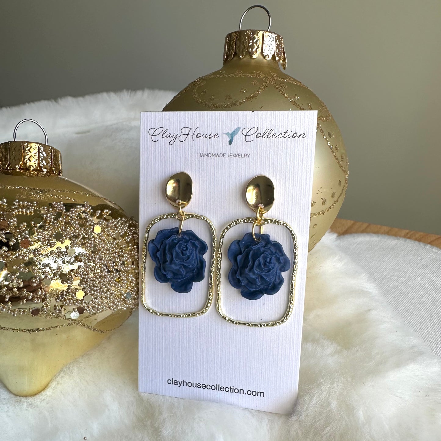 Blue flower earrings on a Clayhouse Collection card with gold ornaments in the background.