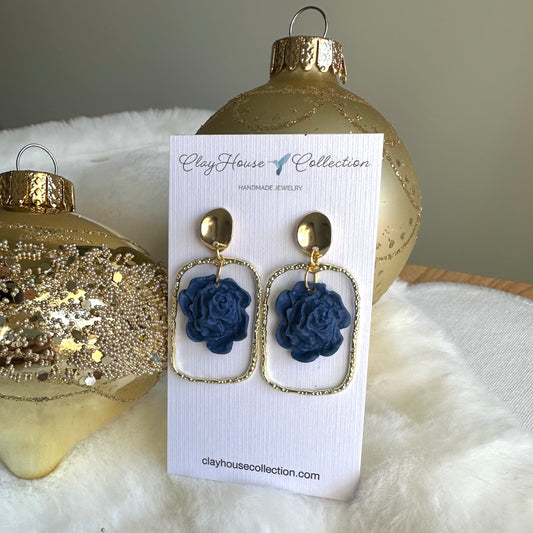 Blue flower earrings on a Clayhouse Collection card with gold ornaments in the background.