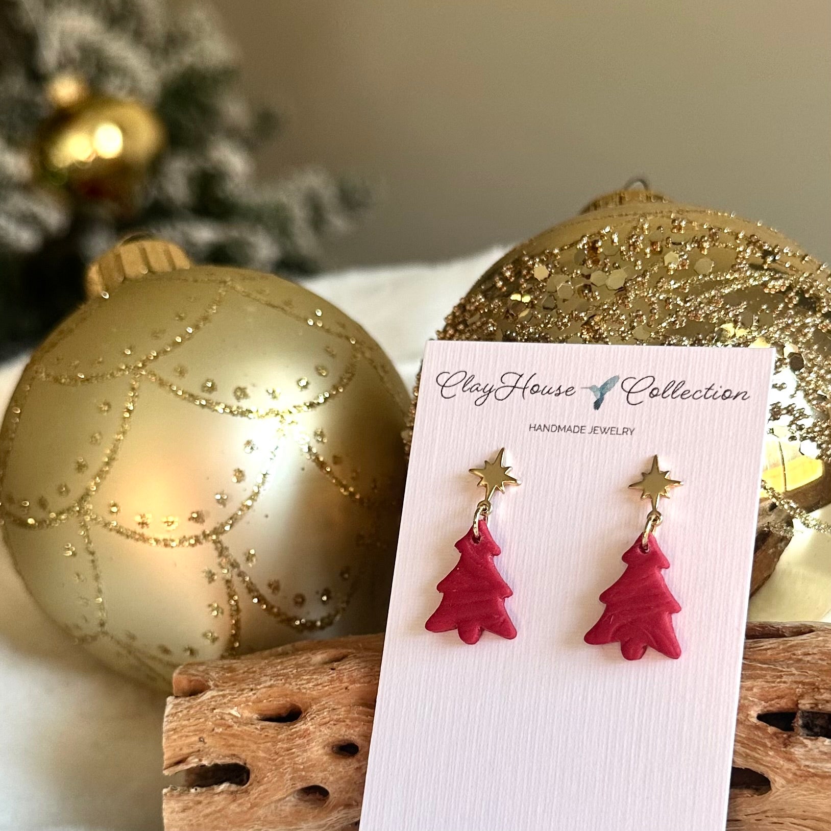 Red Christmas tree earrings on a card with gold ornaments in the background