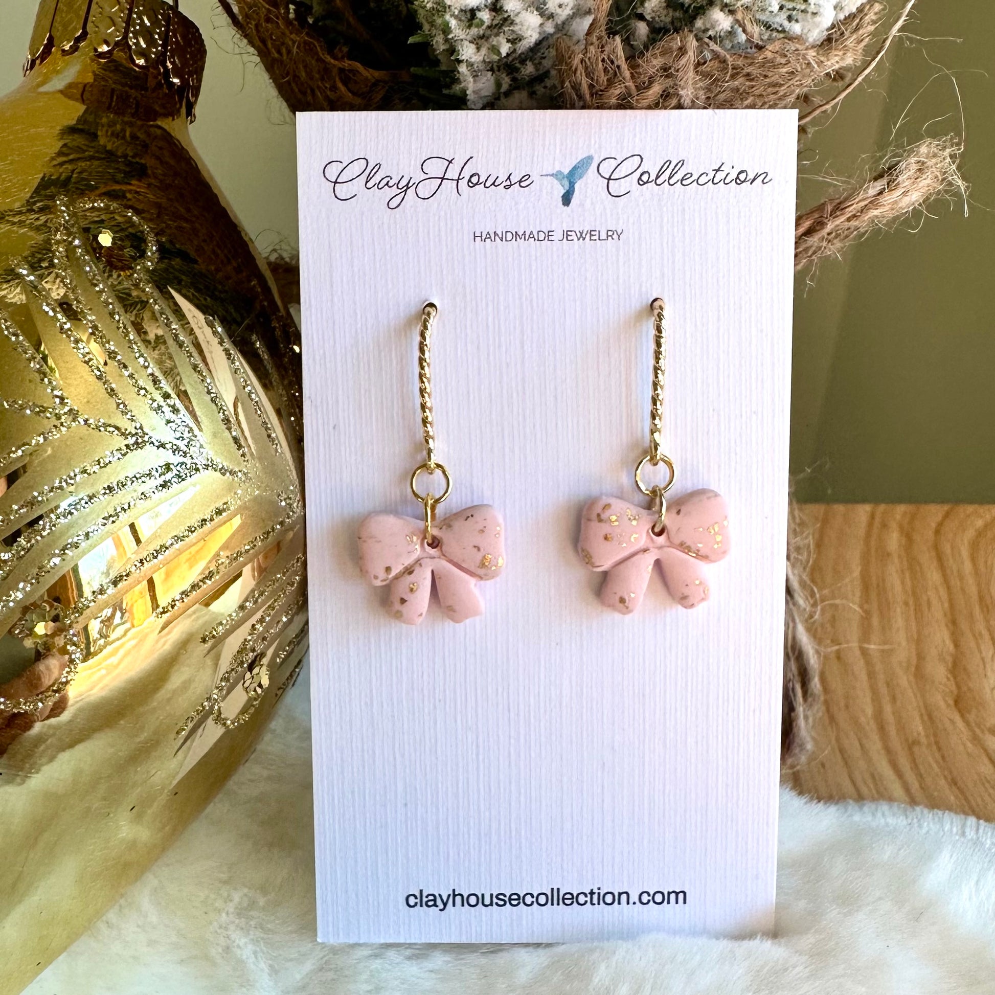 Pink bow-shaped earrings on a ClayHouse Collection card with decorative background