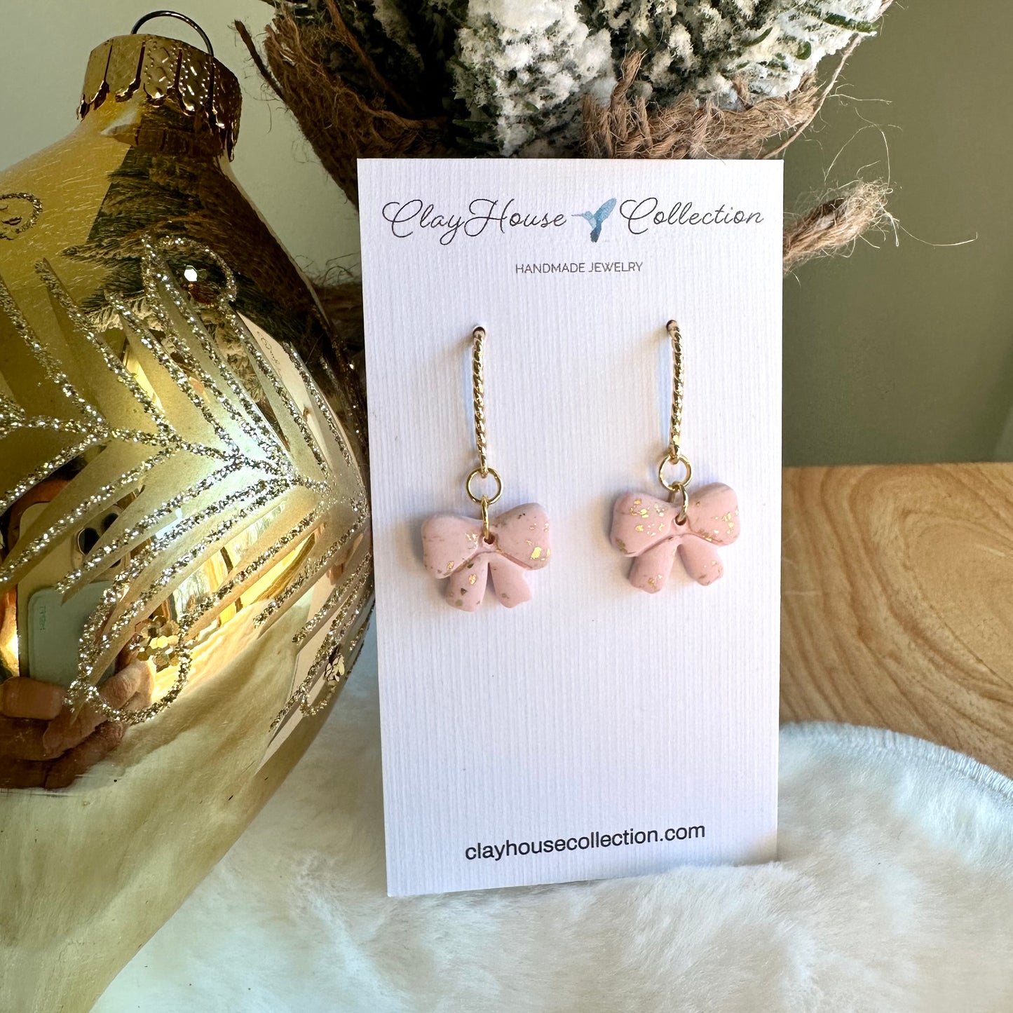 Pink bow-shaped earrings on a ClayHouse Collection card with decorative background