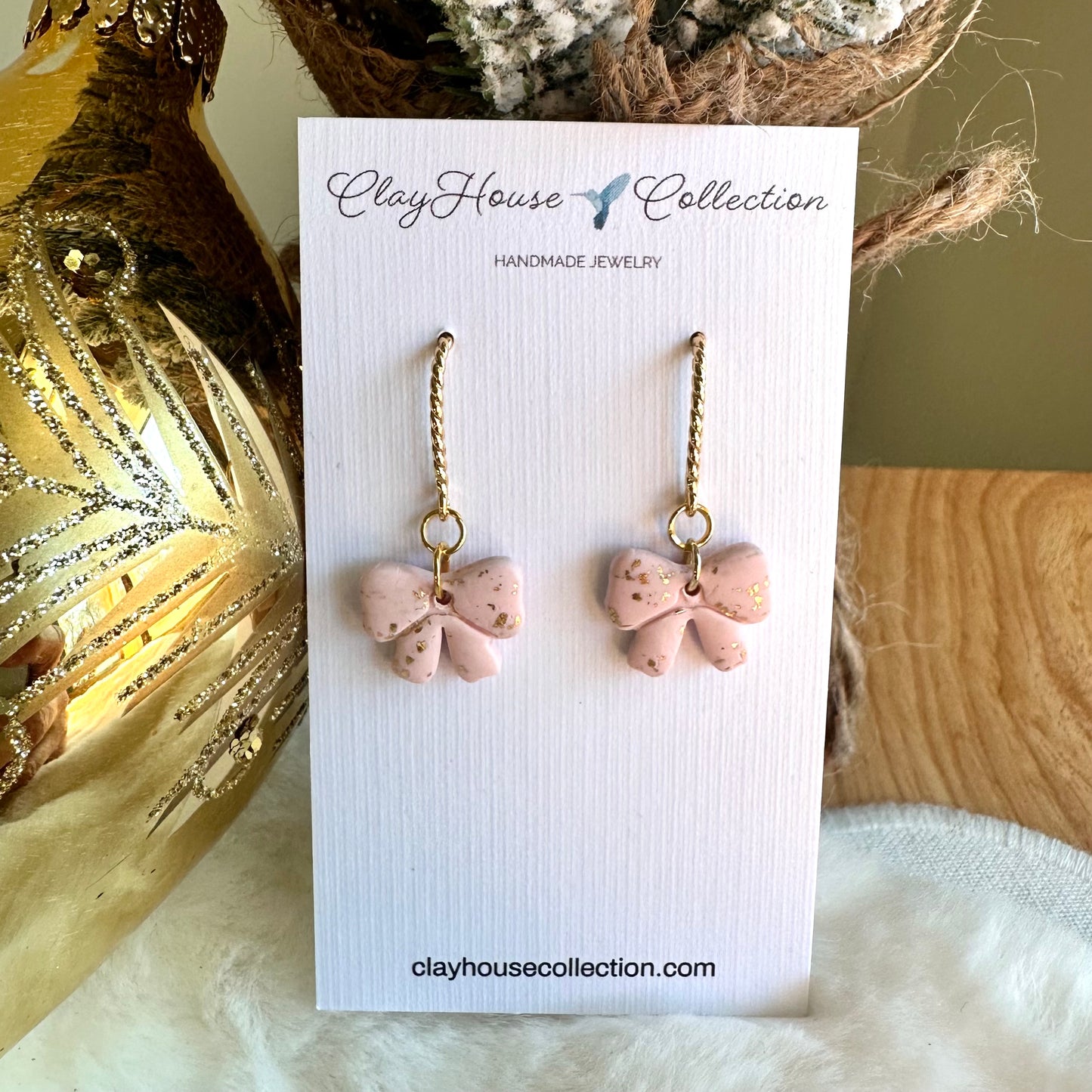 Pink bow-shaped earrings on a ClayHouse Collection card with decorative background